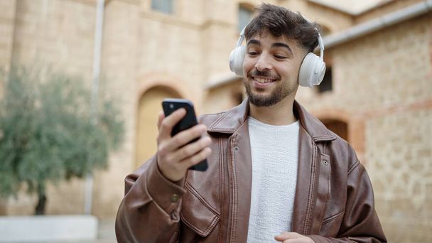 Junger Araber lächelt selbstbewusst und hört Musik auf der Straße - Foto, Bild