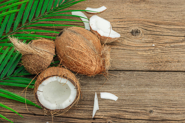 Summer tropical background with coconuts and palm leaves. Traditional decor, textured fruit, voyage concept. Old wooden boards background, flat lay, top view - 写真・画像
