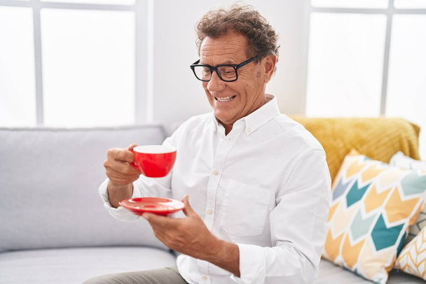 Мужчина средних лет пьет кофе сидя дома на диване - Фото, изображение