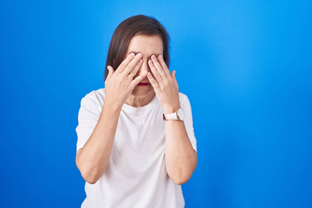 Middle age hispanic woman standing over blue background rubbing eyes for fatigue and headache, sleepy and tired expression. vision problem  - Fotografie, Obrázek