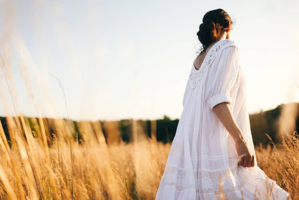 Brunette young woman in wild field. Natural beauty and romance concept. Sunset light. View from the back. - Φωτογραφία, εικόνα