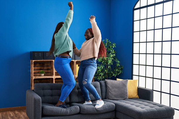 African american women friends smiling confident dancing on sofa at home - 写真・画像