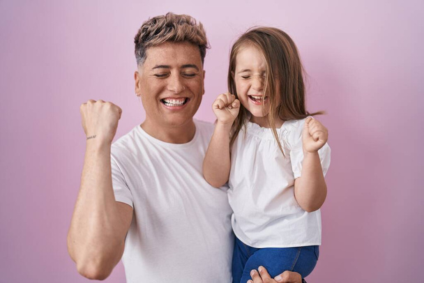 Νεαρός πατέρας αγκαλιάζει την κόρη πάνω από ροζ φόντο ουρλιάζοντας υπερήφανος, γιορτάζει τη νίκη και την επιτυχία πολύ ενθουσιασμένος με σήκωσε τα χέρια  - Φωτογραφία, εικόνα