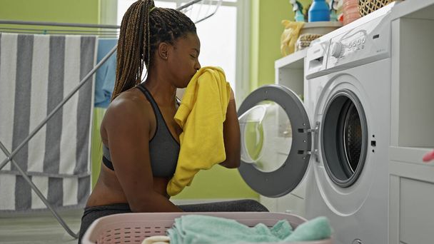 洗濯室で汚れたTシャツの匂いを嗅ぐアフリカ系アメリカ人女性 - 写真・画像