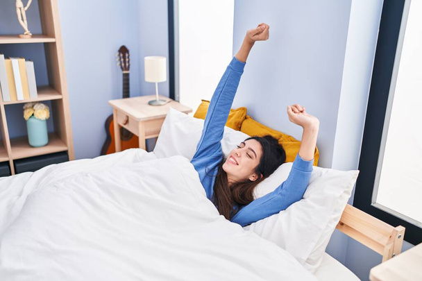 Young beautiful hispanic woman waking up stretching arms at bedroom - Fotoğraf, Görsel