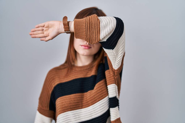 Fiatal gyönyörű nő csíkos pulóvert visel az elszigetelt háttér borító szemét karjával, komoly és szomorú. látástalan, rejtőzködő és elutasító koncepció  - Fotó, kép