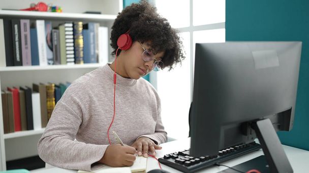 アフリカ系アメリカ人の若い女性が大学の教室でノートにコンピュータライティングを使って - 写真・画像