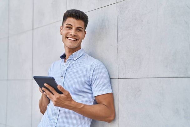 Jovem hispânico sorrindo confiante usando touchpad na rua - Foto, Imagem