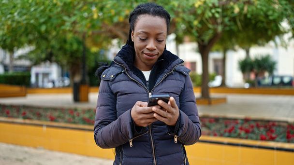 アフリカ系アメリカ人女性が公園でスマートフォンを使って自信を持って笑っている - 写真・画像