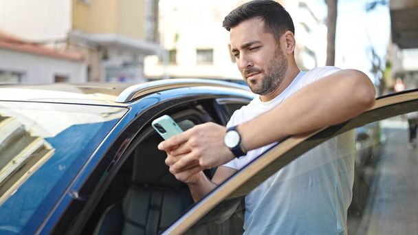 Young hispanic man using smartphone leaning on car at street - Zdjęcie, obraz