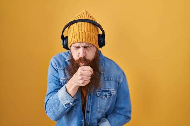 長いひげを持つ白人男性は,ヘッドフォンを使って音楽を聴き,風邪や気管支炎の症状として気分が悪くなったり咳をしたりします. 医療コンセプト.  - 写真・画像