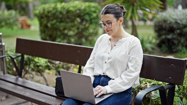 Молода красива іспаномовна жінка використовує ноутбук, сидячи на лавці в парку - Фото, зображення