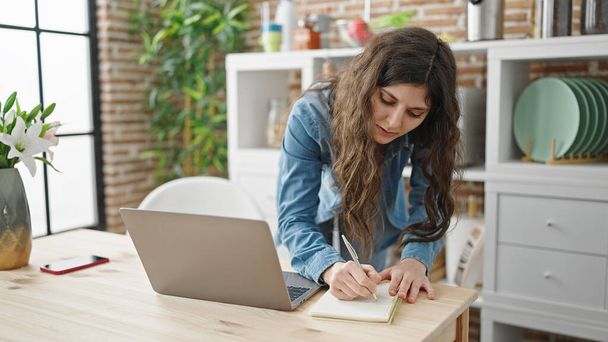 Молода красива іспаномовна жінка використовує ноутбук, пишучи нотатки в їдальні
 - Фото, зображення