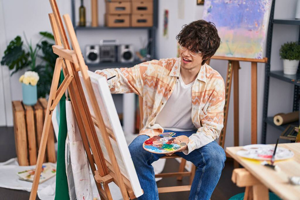 Jonge Spaanse man kunstenaar glimlachend zelfverzekerd tekenen in kunststudio - Foto, afbeelding