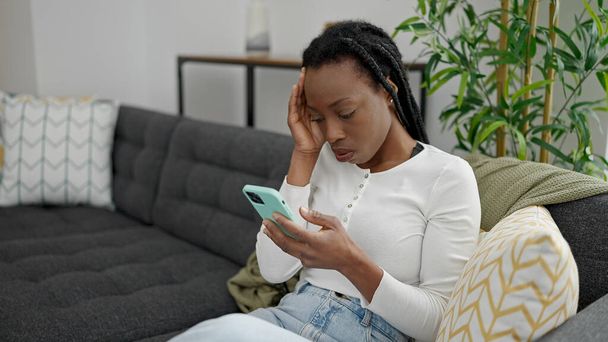 African american woman using smartphone sitting on sofa at home - Photo, Image