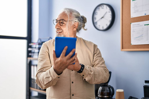 Середнього віку сіро-волохатий чоловік бізнесмен посміхається впевнено використовуючи тачпад в офісі
 - Фото, зображення