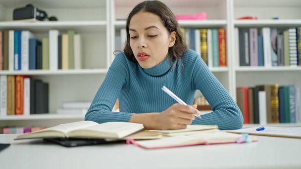 Genç, güzel İspanyol kız öğrenci üniversite sınıfında deftere yazı yazıyor. - Fotoğraf, Görsel