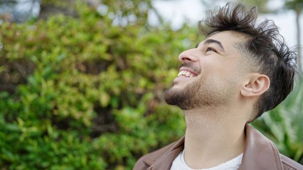 Junger arabischer Mann lächelt zuversichtlich in den Himmel im Park - Foto, Bild