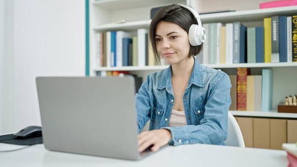 Jovem estudante caucasiana usando computador usando fones de ouvido na sala de aula da universidade - Foto, Imagem