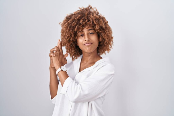 Young hispanic woman with curly hair standing over white background holding symbolic gun with hand gesture, playing killing shooting weapons, angry face  - Photo, Image