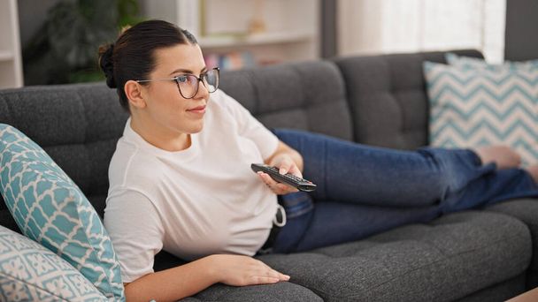 Fiatal gyönyörű spanyol nő néz TV-t feküdt kanapén otthon - Fotó, kép