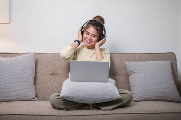 Porträt einer jungen Asiatin, die gerne Musik mit Kopfhörern hört und Laptop benutzt, fröhliche und entspannende Zeit.. - Foto, Bild