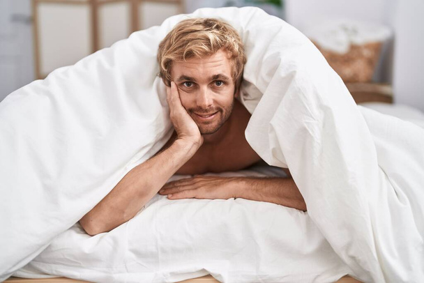 寝室のベッドに横たわるベッドシートで覆っている若い男 - 写真・画像