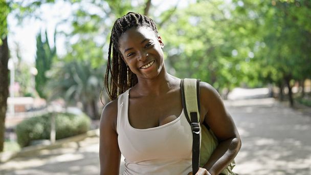 Αφροαμερικανή τουρίστρια φορώντας σακίδιο χαμογελώντας στο πάρκο - Φωτογραφία, εικόνα