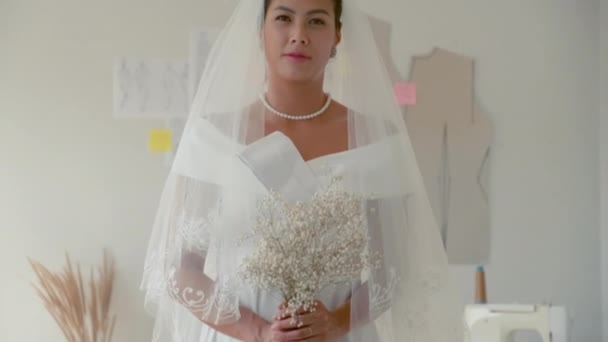 Tilt up portrait of happy bride in elegant white wedding dress and veil posing for camera in studio - Footage, Video
