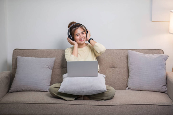 Portret van jonge Aziatische vrouw genieten van het luisteren naar muziek met hoofdtelefoon en met behulp van laptop, gelukkige en ontspannen tijd.. - Foto, afbeelding