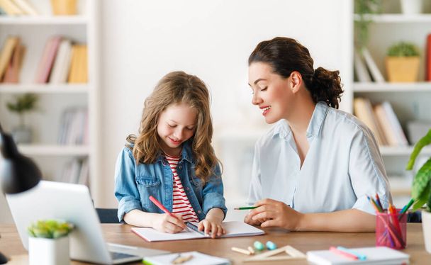 Happy child and adult are sitting at desk. Girl doing homework or online education. - Foto, Bild