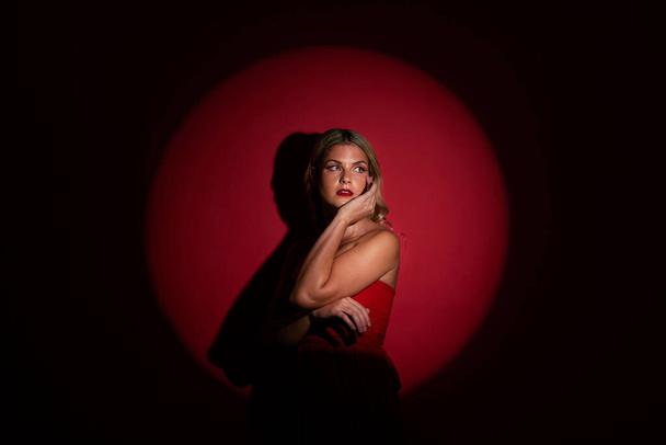 Fashion, spotlight and red with a model woman in studio on a dark background for classy elegance or style. Beauty, aesthetic and luxury with a confident young female person standing in a dress. - Фото, зображення