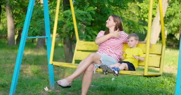 Щаслива сім'я, мати і дитина гойдаються на гойдалці в міському парку. Концепція щасливої сім'ї, снів, розваг. Мама і син разом. Кадри високої якості 4k - Кадри, відео