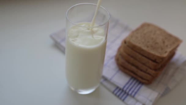 In Zeitlupe Milch in Glas auf dem Küchentisch gießen. Glas frische Milch mit Sauerteigbrot zum Frühstück - Filmmaterial, Video