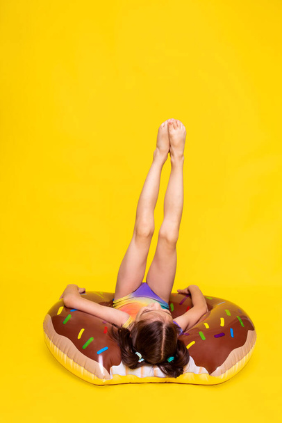 girl in swimsuit lay on inflatable ring and keeps legs up, resting and relaxing in summer - Φωτογραφία, εικόνα