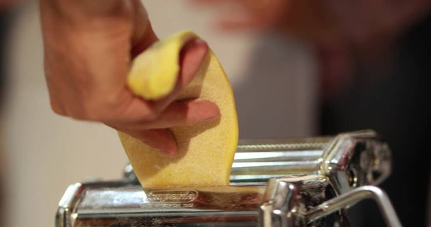 Haciendo pasta casera. Utilizando una máquina de pasta, el chef prepara la pasta a mano. Transformando la masa en delicadas cintas de pasta. - Foto, imagen