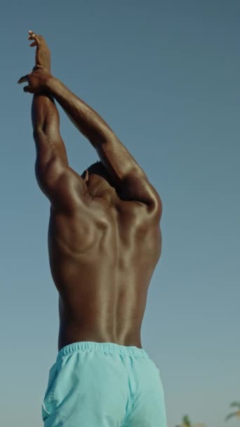 Vídeo vertical en cámara lenta de la vista trasera de un hombre africano fuerte que se extiende al aire libre - Imágenes, Vídeo