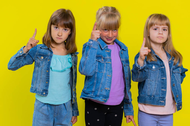 Quarrel. Displeased teenage girls gesturing hands with irritation and displeasure, blaming scolding for failure, asking why this happened. Children sisters. Three siblings kids on yellow background - Photo, Image