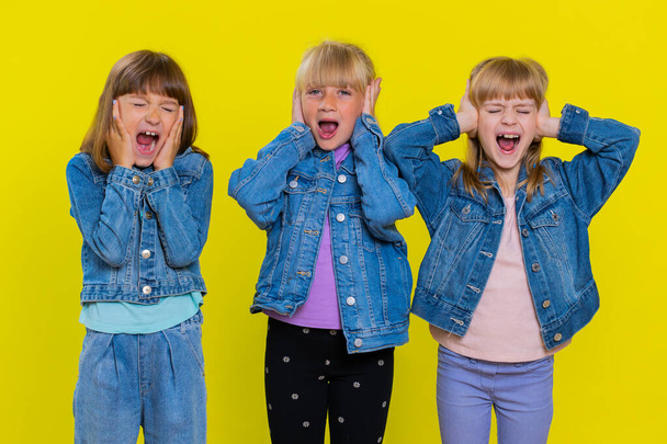 Teenage girls screams from stress tension problems feels horror hopelessness fear surprise shock expresses gestures rage. Children sisters. Three siblings kids isolated on studio yellow background - Photo, Image