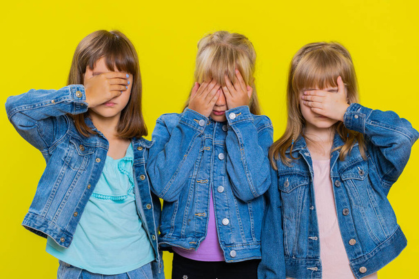 Dont want to look at this, awful. Teenage girls closing eyes with hand showing stop gesture, confused shy scared to watch. Little children sisters. Three siblings kids isolated on yellow background - Fotografie, Obrázek
