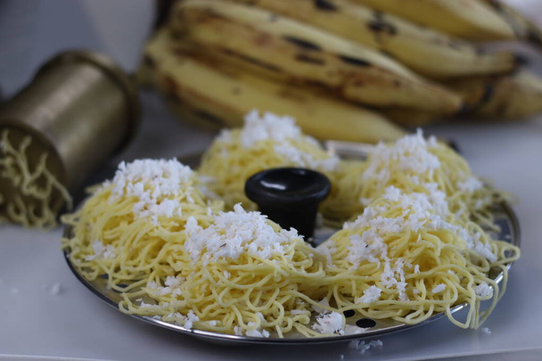 Ethakka idiyappam geserveerd in de ijdele mal. Snijtrechters of idiyappam gemaakt met rijstmeel deeg gemengd met gestoomde weegbree. Schot met traditionele idiyappam pers en rijpe weegbree - Foto, afbeelding