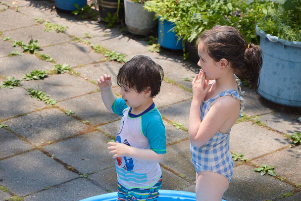 Siblings playing in a shallow pool in the backyard - Foto, Imagen