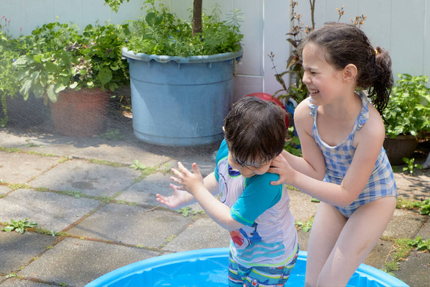 sisarukset leikkivät vedellä takapihalla kuumana kesäpäivänä - Valokuva, kuva