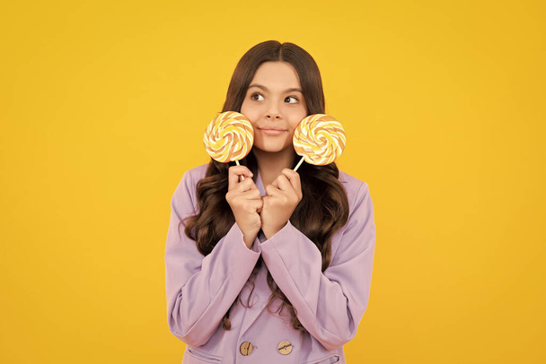 Teenager girl eating sugar lollypop. Candy and sweets for kids. Child eat lollipop popsicle over yellow isolated background. Yummy caramel, candy shop - Foto, Imagen