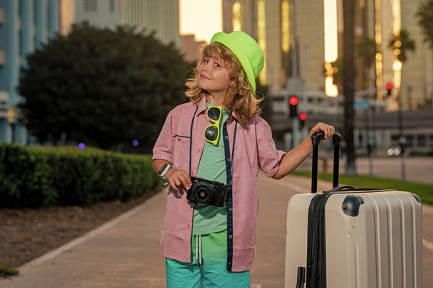 Kinder reisen. Glücklicher Junge mit Reisekoffern auf der Straße der Stadt. Lebensstil und Reiseträume - Foto, Bild