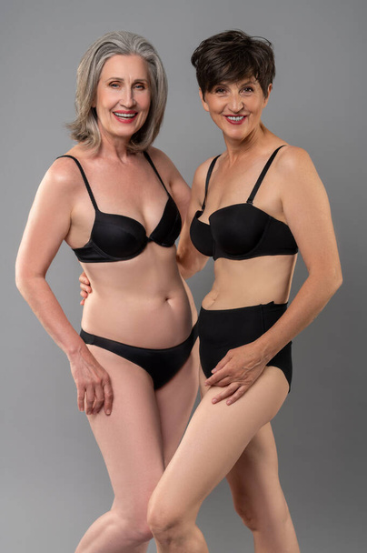 Women in lingerie. Two senior women in balck lingerie standing close - Foto, Imagem