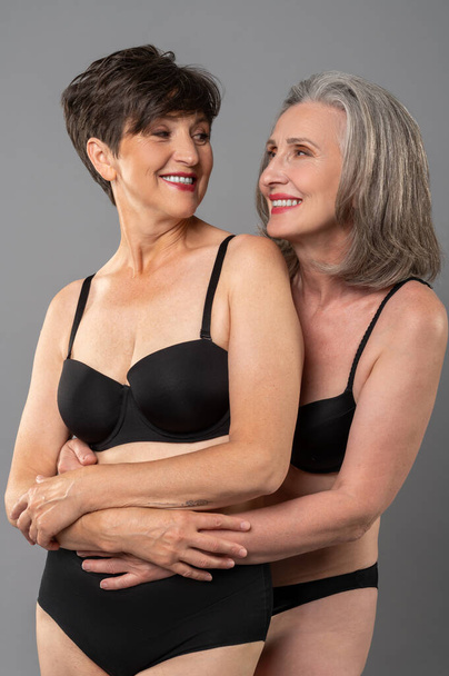 Body positivity. Senior woman in black lingerie feeling good and smiling - Foto, afbeelding