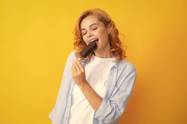 Sommerkonzept. Froh positive Frau hält leckeres gefrorenes Eis, genießt leckeres kaltes Dessert, posiert auf gelbem Hintergrund, fühlt sich glücklich - Foto, Bild