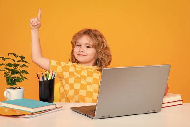Παιδί του σχολείου κρατώντας δείκτη επάνω με μεγάλη νέα ιδέα. Nerd μαθητής αγόρι από το δημοτικό σχολείο με το βιβλίο απομονώνονται σε κίτρινο φόντο στούντιο. Μαθητής που χρησιμοποιεί φορητό υπολογιστή - Φωτογραφία, εικόνα