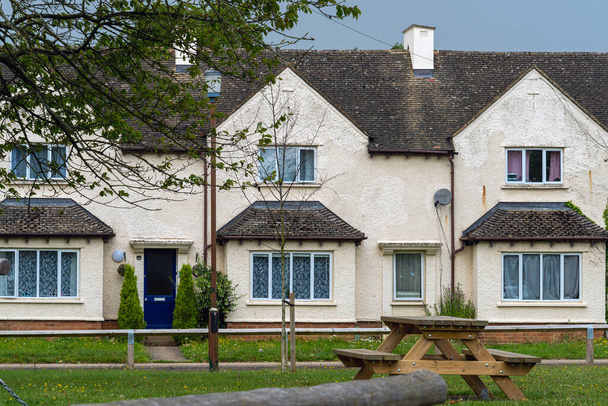Elbűvölő angol vidéki ház, zöld környezet, felhős ég. Fából készült asztal és faágak az előtérben. Fenntartható építészet és tervezés. - Fotó, kép
